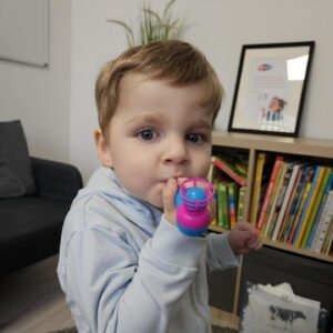 Chłopiec podczas terapii logopedycznej dmucha w zabawkę logopedyczną z piłeczką